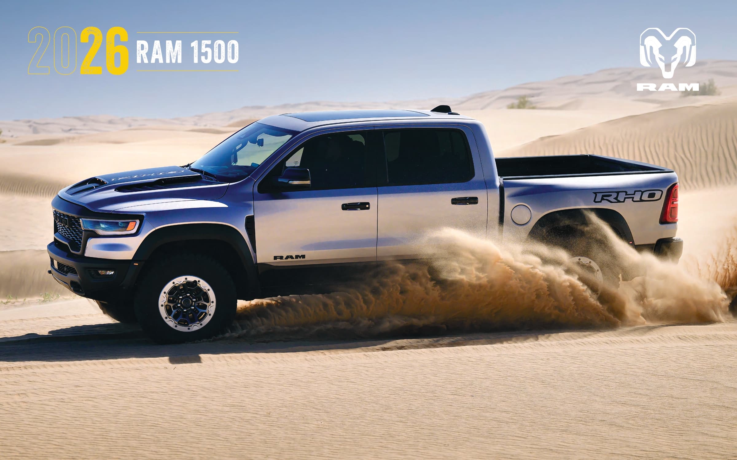 2026 Ram 1500 truck drives through sandy desert, showcasing off-road capability and rugged design.